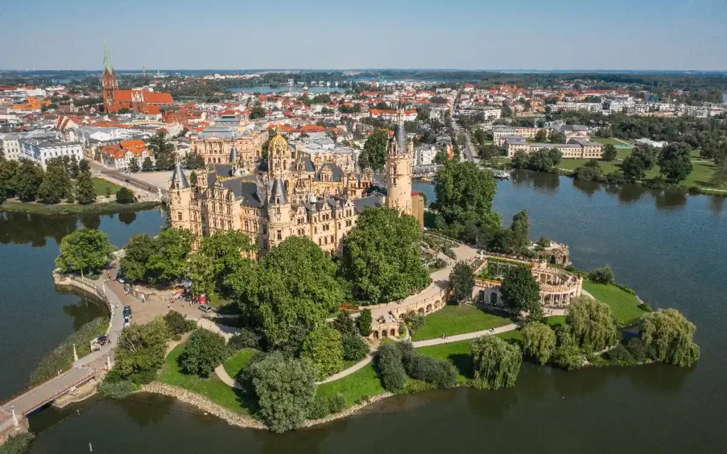 Aerial view of a stunning castle surrounded by water and lush greenery, showcasing a picturesque landscape in a city.