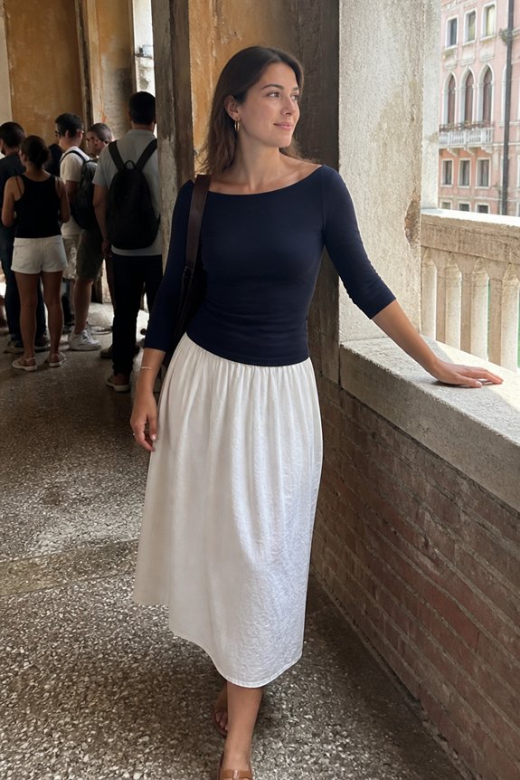 Woman in navy top and white midi skirt leaning on a stone balcony at a historic site, with tourists in the background.