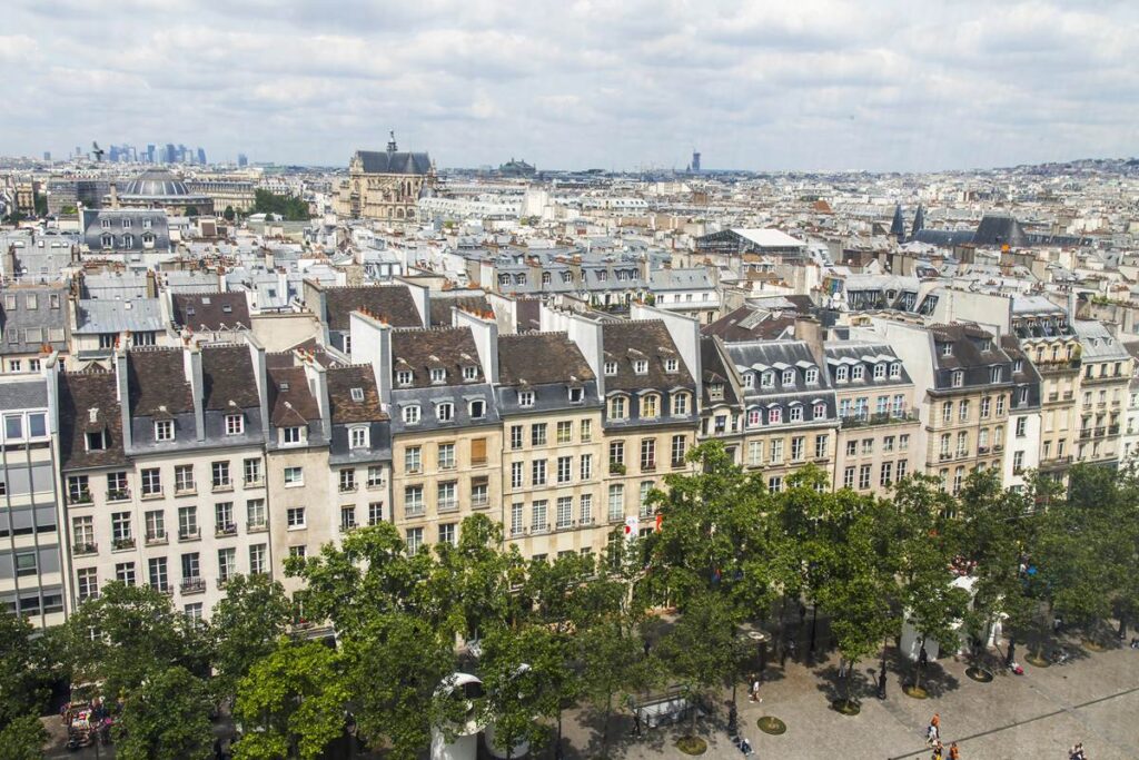 Aerial view of historic Parisian architecture with tree-lined streets and cloudy sky.