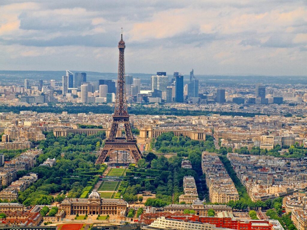 Aerial view of the Eiffel Tower in Paris, surrounded by cityscape and greenery under a cloudy sky.