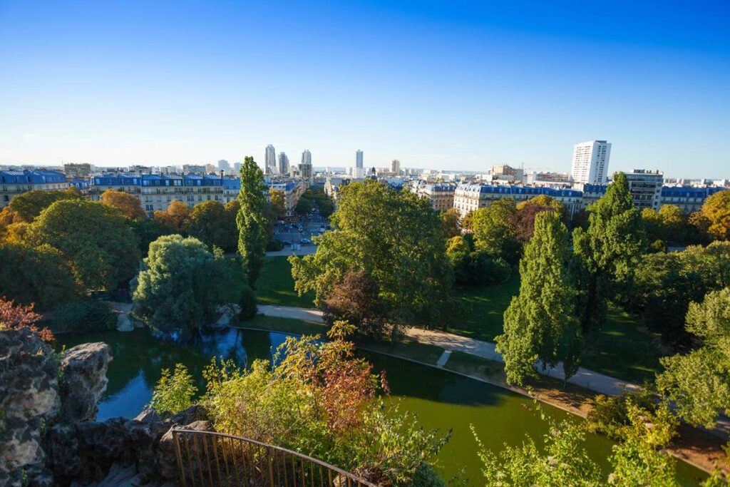 View of lush green park in Paris with trees and cityscape under clear blue sky.