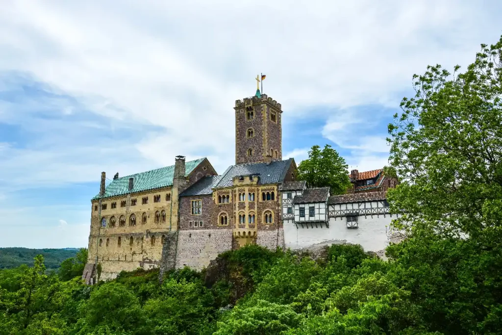 Alt text: Historic castle with a tall tower surrounded by lush greenery under a blue sky, showcasing its medieval architecture.