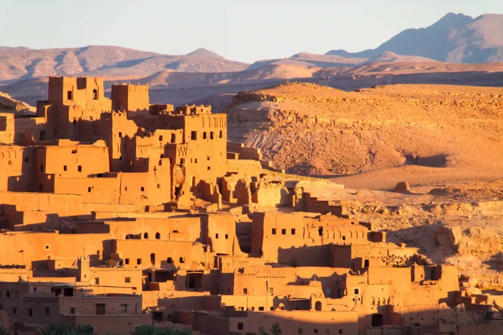 Sunset view of ancient adobe buildings in a desert landscape, showcasing rich textures and mountainous backdrop.