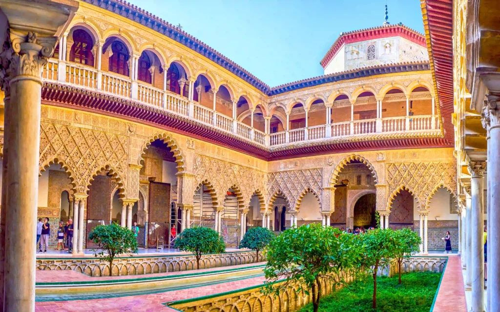 Intricate courtyard architecture with lush greenery and visitors at a historic building featuring Moorish design elements.