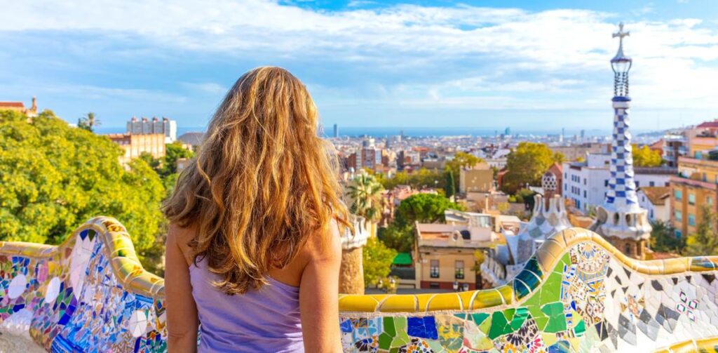 Woman overlooks colorful cityscape from Park Güell in Barcelona, highlighting vibrant architecture and scenic views.