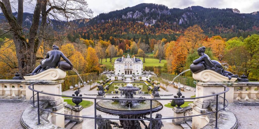 Elegant palace garden with fountains and autumn colors, framed by scenic mountains in the background.