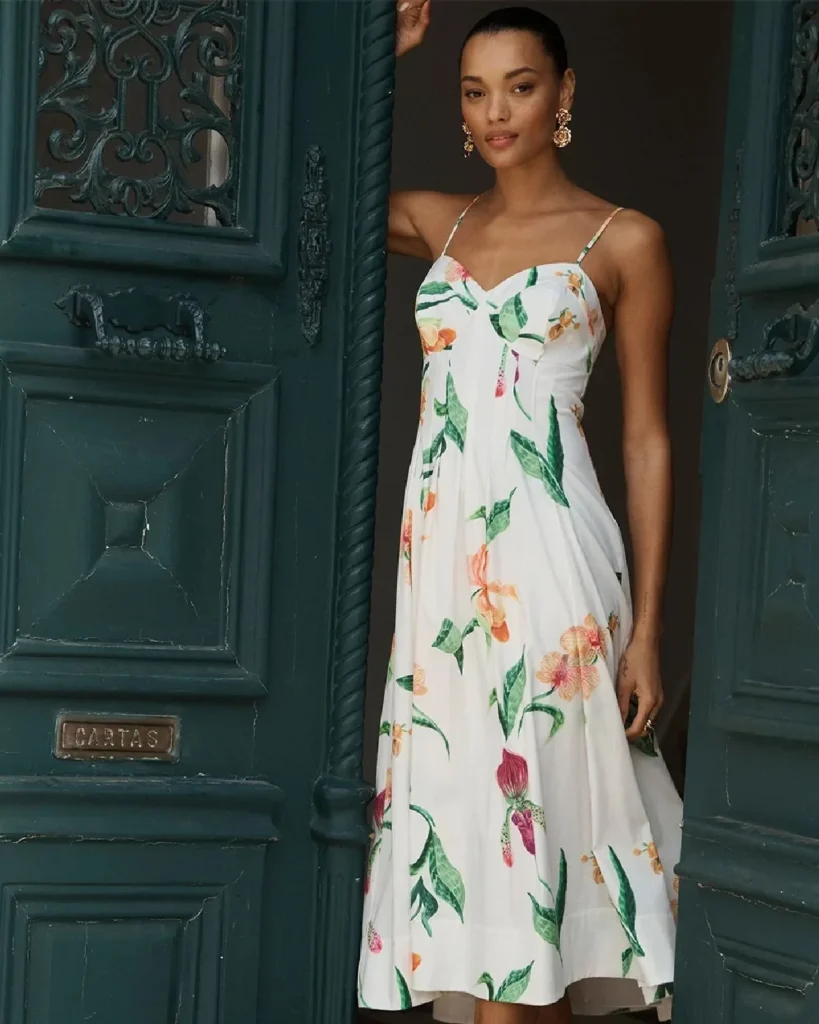 Model in floral summer dress standing in an ornate doorway, showcasing a stylish and vibrant fashion look.