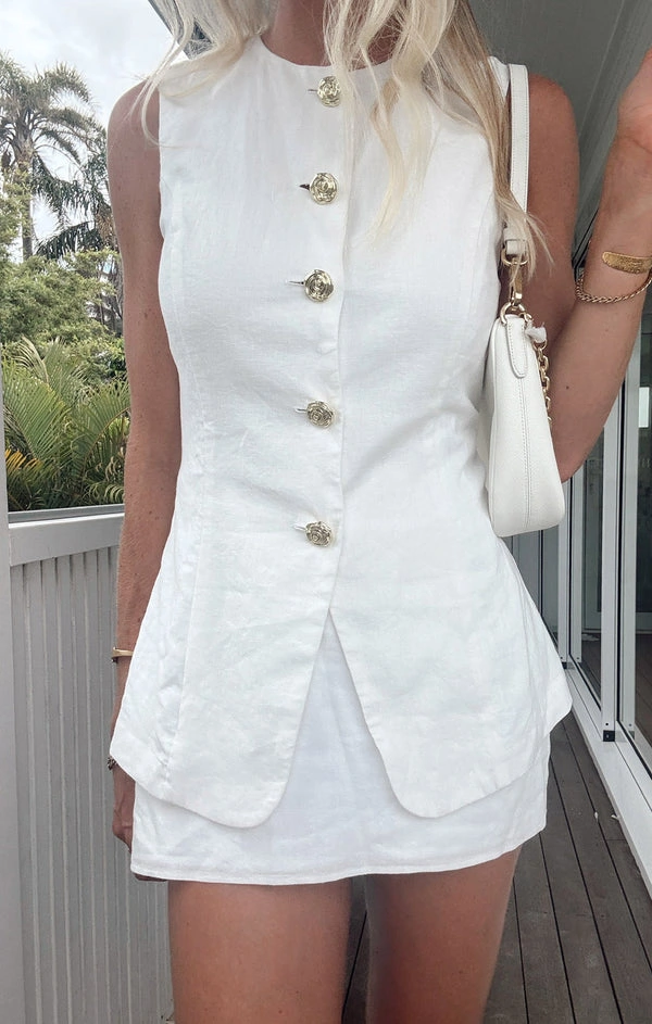 Stylish woman in a white button-front dress with a chic handbag, standing on a deck surrounded by greenery.