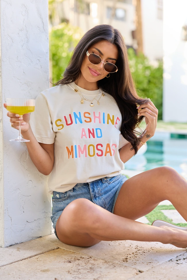 Woman in sunglasses holding a drink, wearing a Sunshine and Mimosas t-shirt by a poolside. Summer vibes and relaxation.