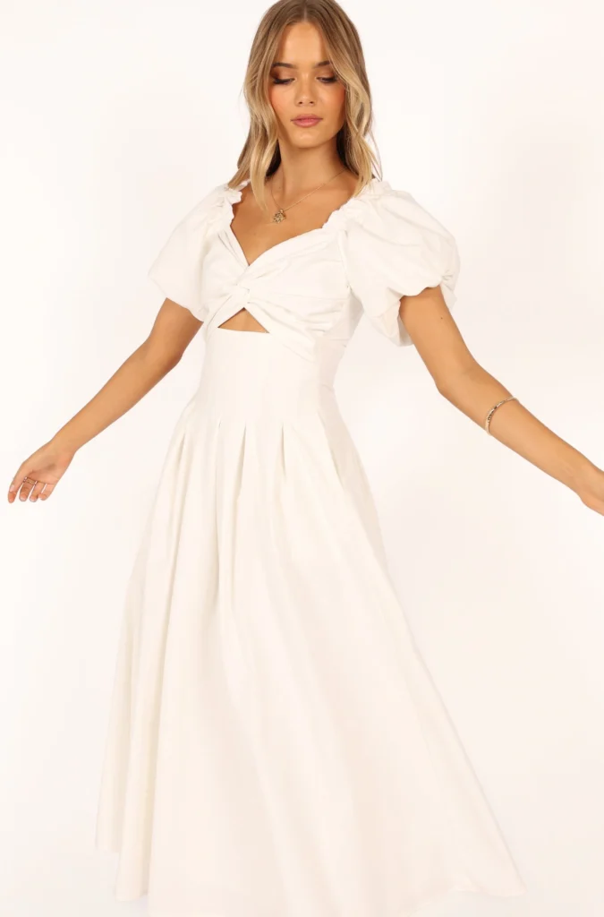 A model showcases a stylish white dress with puff sleeves and a tied waist, perfect for elegant occasions.