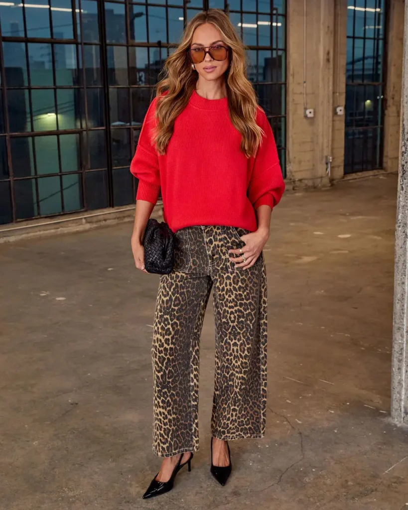 Chic woman in a red sweater and leopard print pants poses confidently in an industrial-style setting.