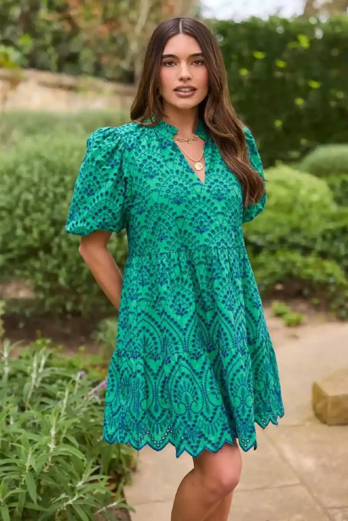 Young woman in a vibrant green patterned dress posing outdoors with lush greenery in the background. Fashionable and stylish look.