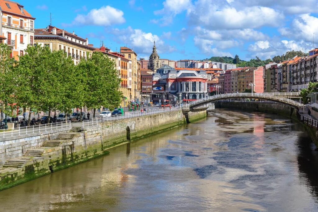 Sunny day view of Bilbao's Casco Viejo, Ría de Bilbao, and architecture with a classic stone bridge.