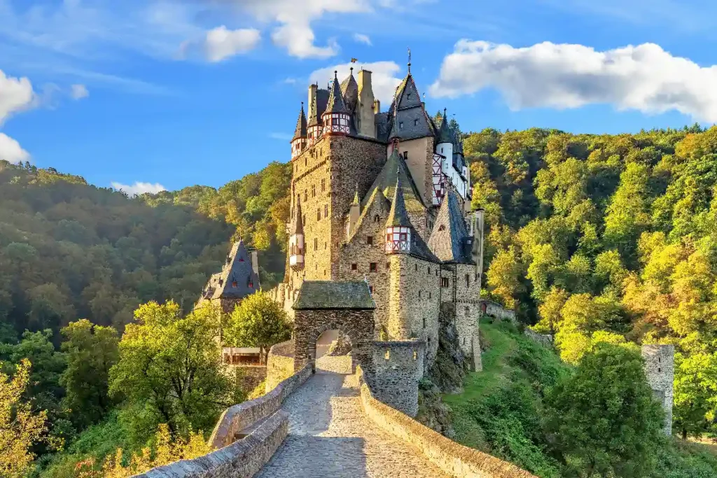 Majestic stone castle surrounded by lush green hills under a blue sky, showcasing medieval architecture and natural beauty.