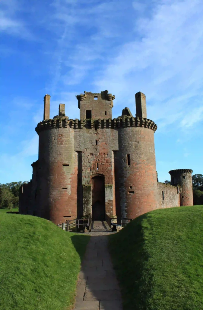 Historic castle surrounded by lush greenery and under a blue sky, showcasing medieval architecture and stonework.