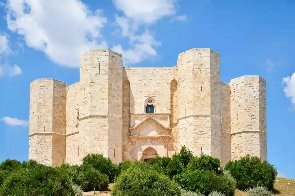 Alt text: The stunning Castel del Monte, an iconic 13th-century castle in Italy, surrounded by lush greenery and blue skies.