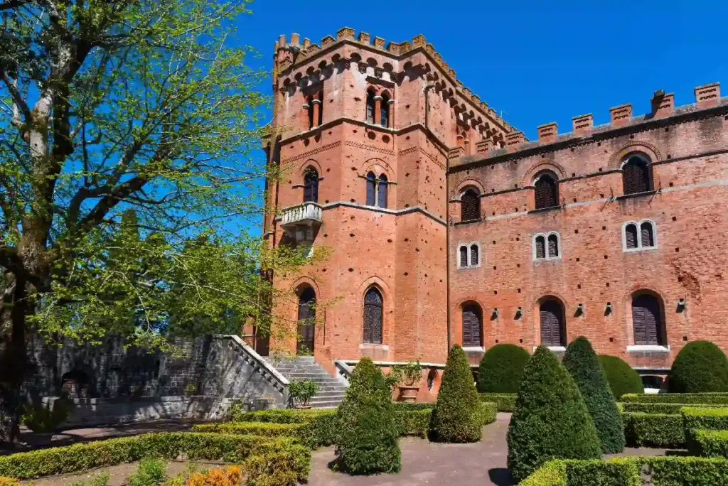 Historic red brick castle surrounded by manicured gardens and blue skies, showcasing architectural beauty and nature.