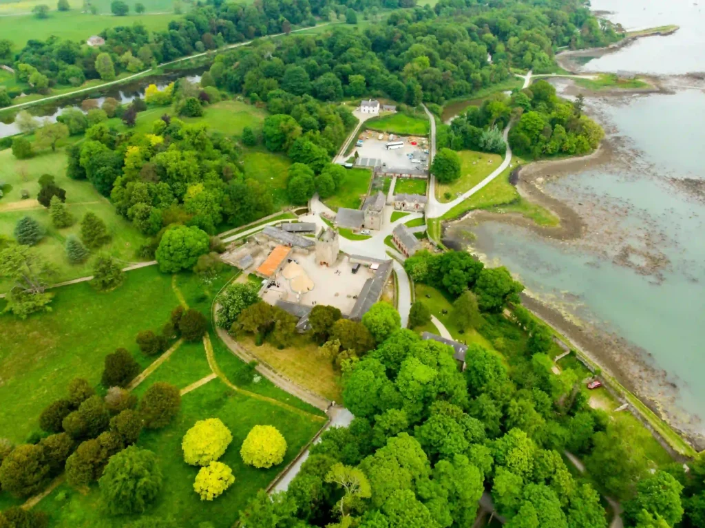 Aerial view of a lush green landscape featuring a historical site and winding pathways near the water's edge.