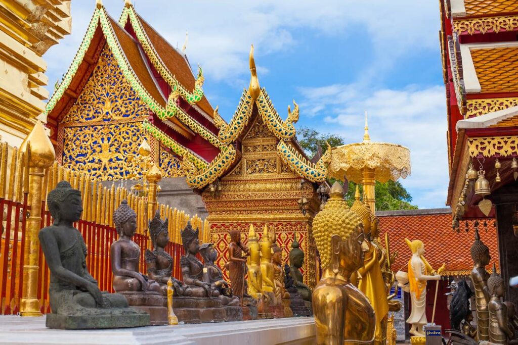 Golden Buddha statues at ornate Thai temple with intricate architectural details under a blue sky.