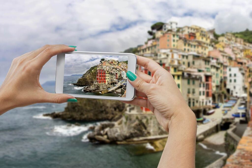 Person photographing colorful seaside buildings on a smartphone, capturing scenic coastal view.
