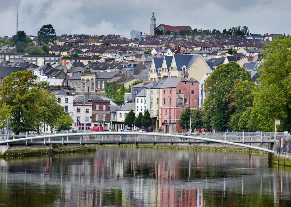 Scenic view of Cork, Ireland with colorful buildings and a riverside bridge on a cloudy day.