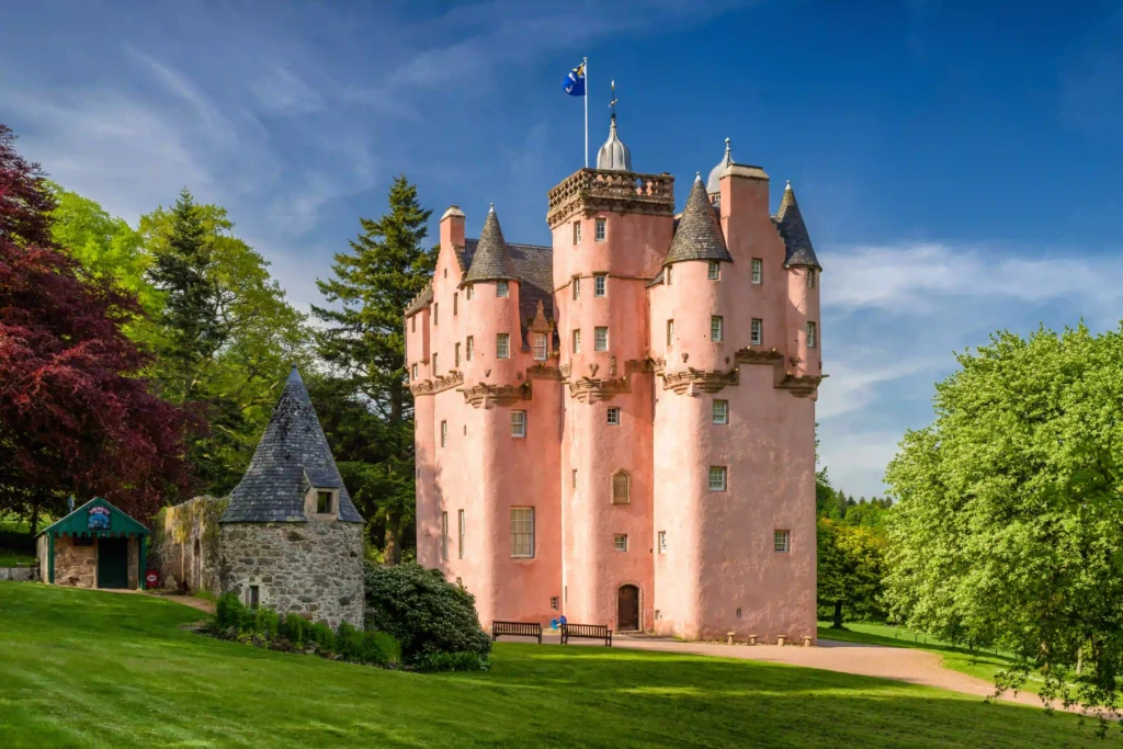 Historic pink castle surrounded by greenery, showcasing unique architecture under a clear blue sky.