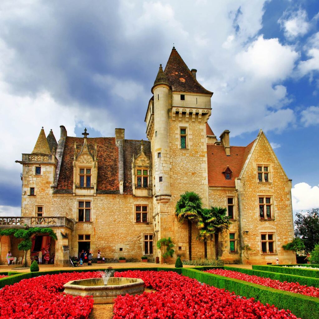 Historic stone castle with vibrant gardens and fountain under a dramatic sky.