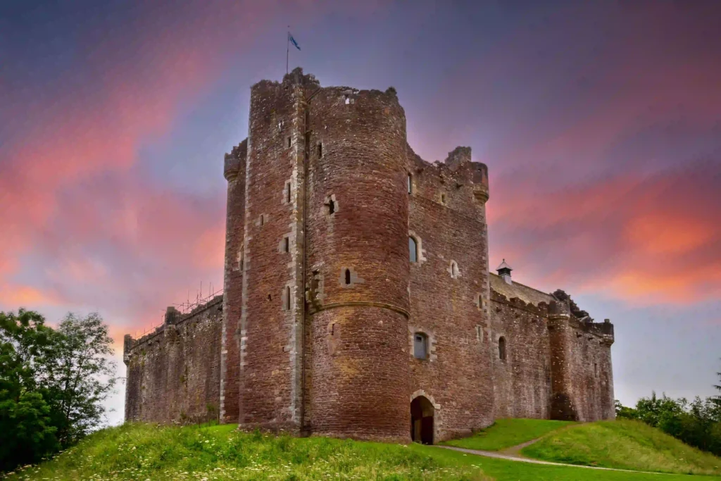 Majestic castle on a grassy hill under a colorful sunset sky, showcasing historic architecture and natural beauty.