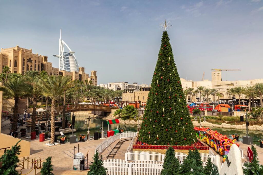 Large Christmas tree near a luxury hotel in a sunny city with palm trees and festive decorations.
