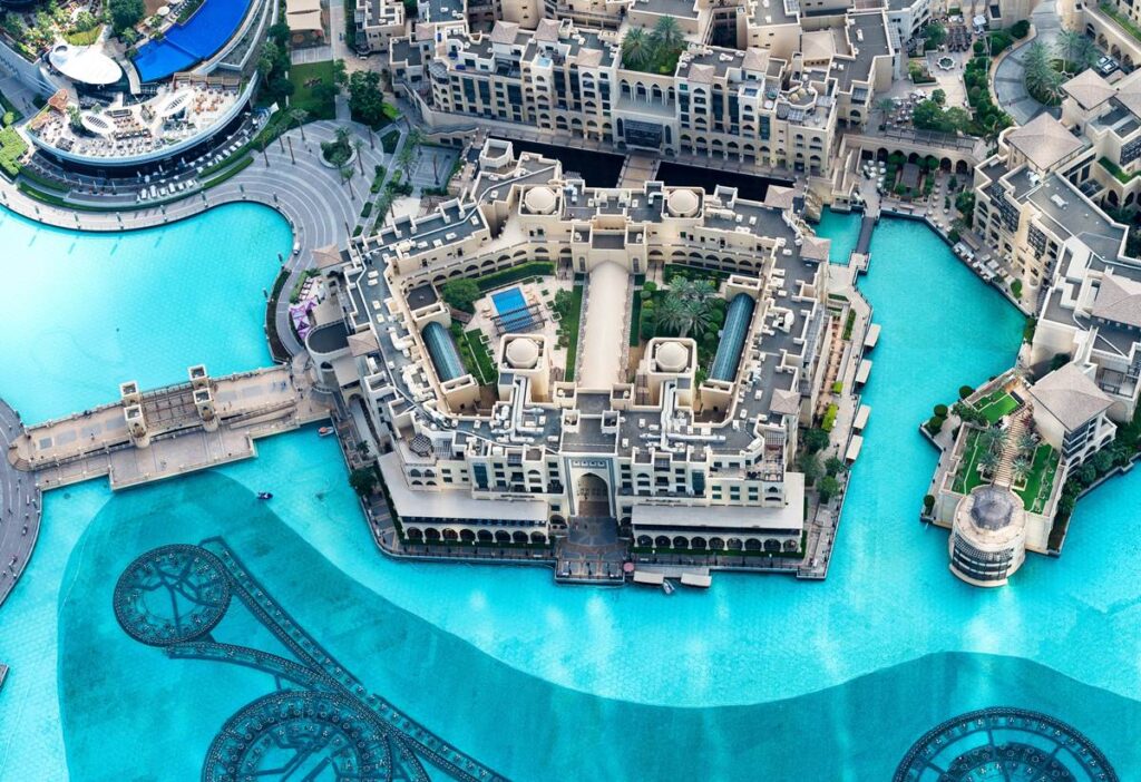 Aerial view of a luxurious resort by a large turquoise lagoon, featuring intricate architectural details and gardens.