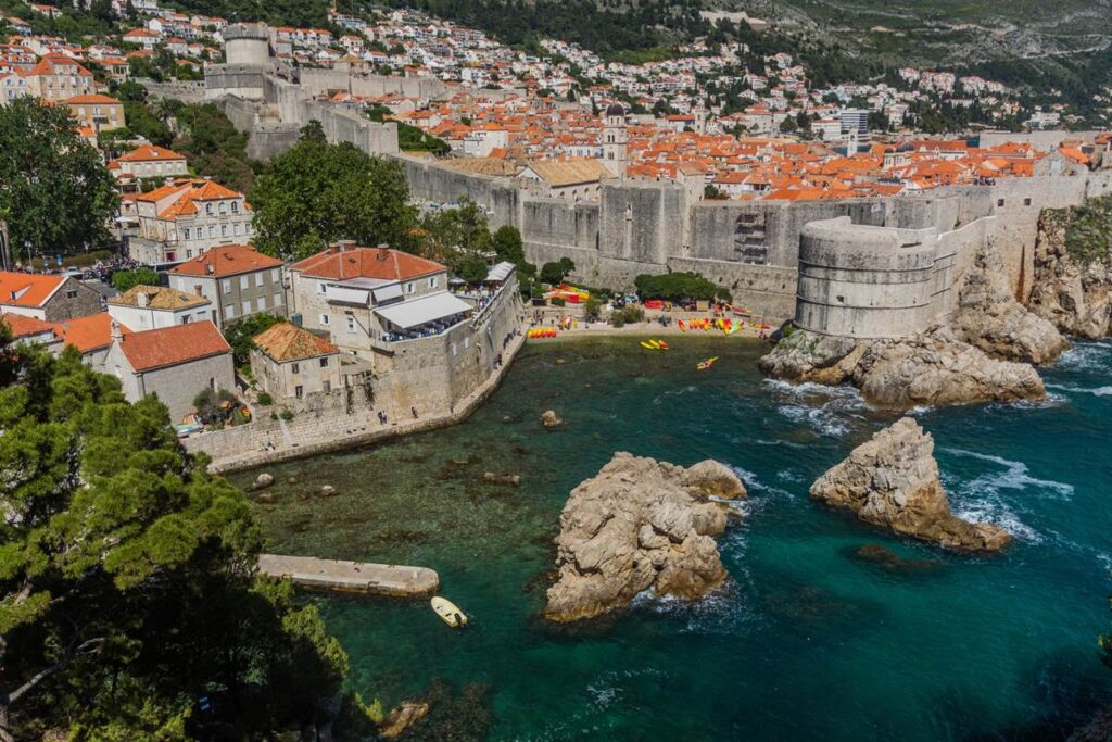Scenic view of Dubrovnik's medieval city walls and turquoise Adriatic Sea, with historic buildings and kayaks.