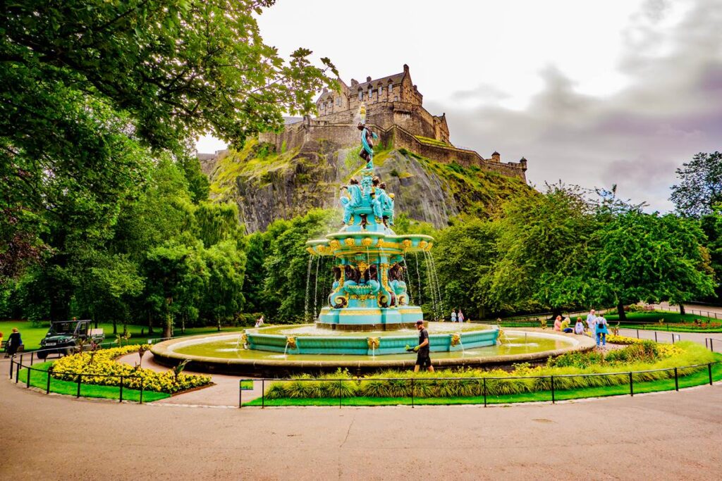 Colorful fountain with castle on hill, surrounded by lush greenery, overcast sky. Scenic view perfect for tourism content.