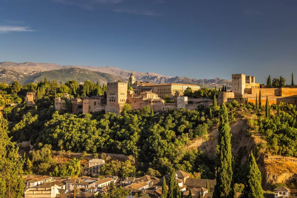 Historic Alhambra Palace in Granada, Spain, with stunning hillside view and vibrant greenery under a clear blue sky.