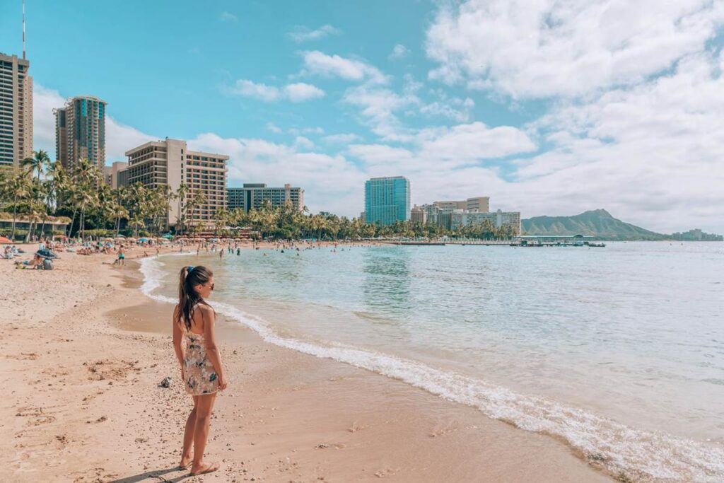 Woman enjoys sunny Waikiki Beach, with skyscrapers and Diamond Head in the background.