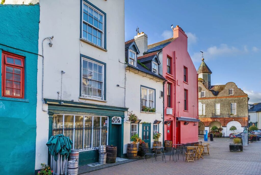 Colorful European street view with vibrant buildings, outdoor tables, and clear blue sky.