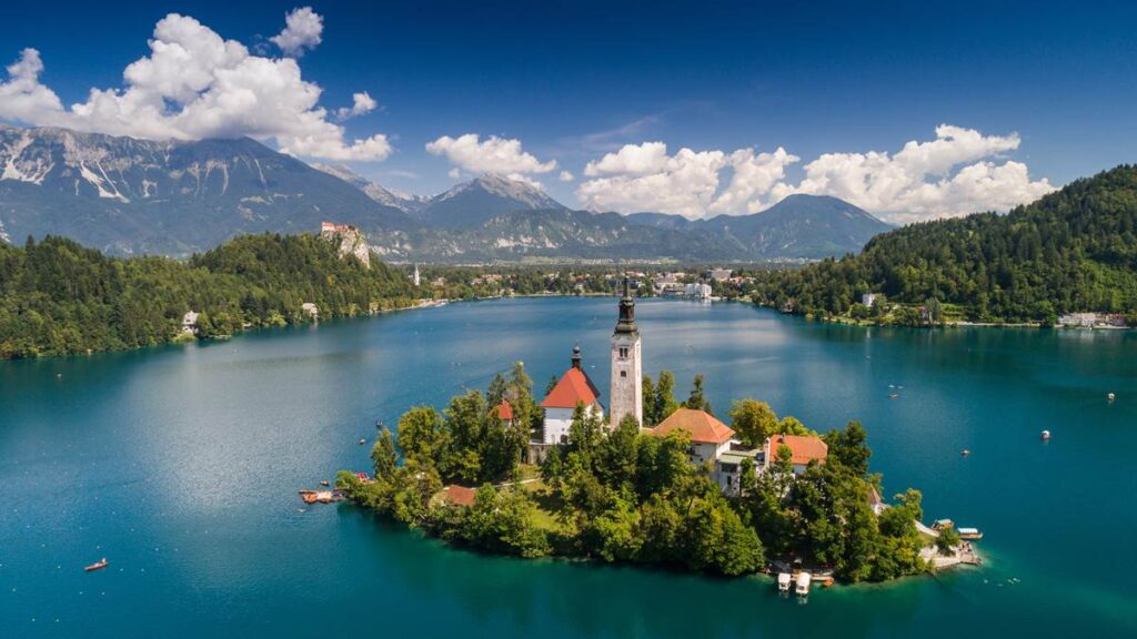 Aerial view of Bled Island with church, surrounded by Lake Bled, Slovenia, mountains and clouds in the background.