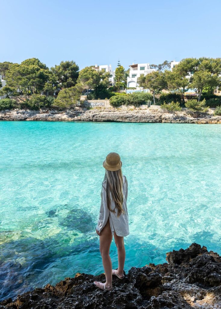 Woman in straw hat enjoying scenic view of turquoise water and coastal homes in the background.
