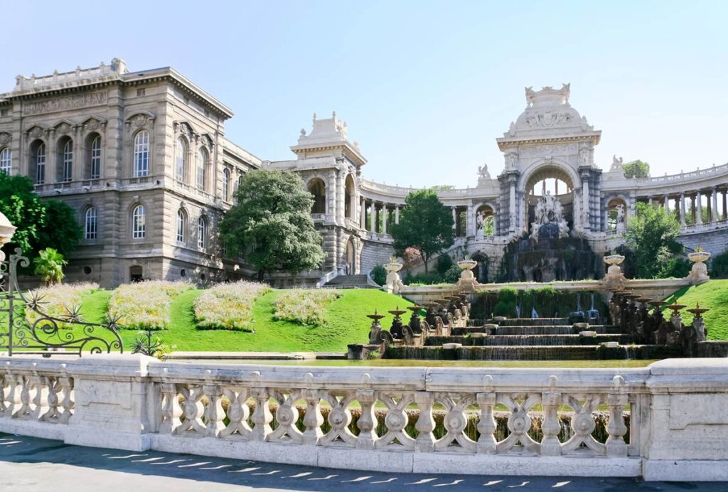 Grand architectural monument with fountain and gardens under a blue sky at Palais Longchamp, Marseille.