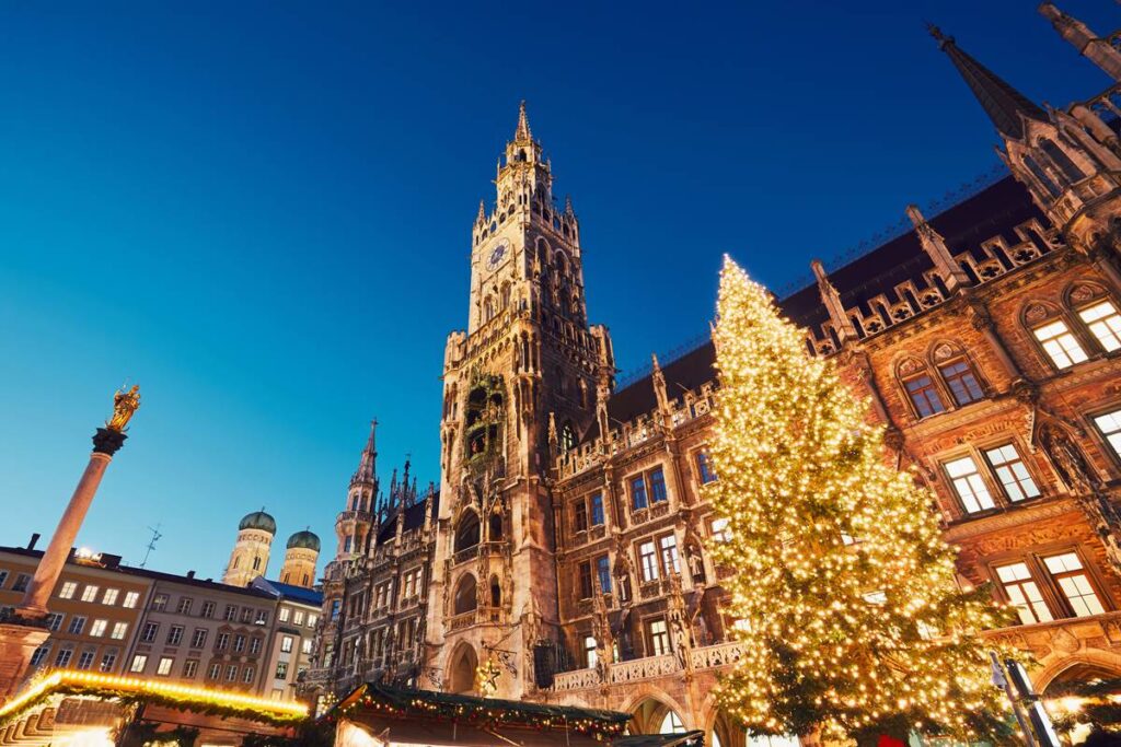Illuminated Christmas tree in front of Munich's historic city hall at dusk.