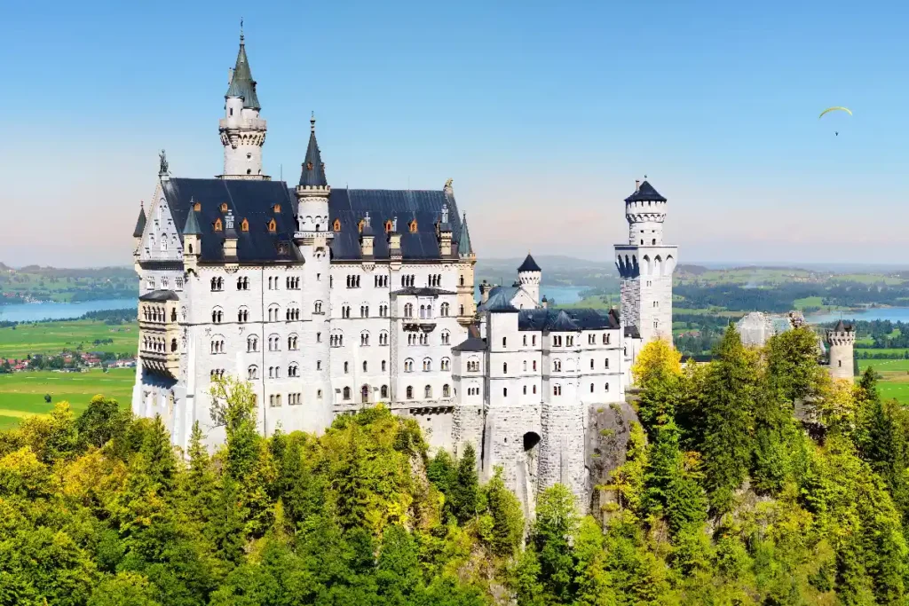Majestic Neuschwanstein Castle in Bavaria, surrounded by lush greenery and scenic landscapes against a clear blue sky.