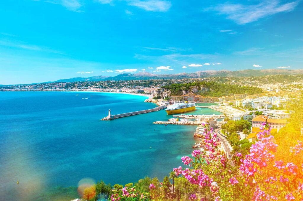 Scenic view of Nice, France coastline with clear blue sky, vibrant flowers, and a harbor.
