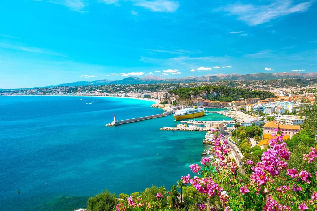 Coastal cityscape of Nice, France with vibrant flowers, blue sea, and a bright sunny sky.
