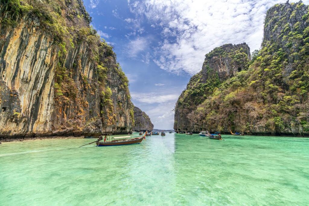Emerald waters and long-tail boats between towering cliffs under a bright sky in a tropical paradise.