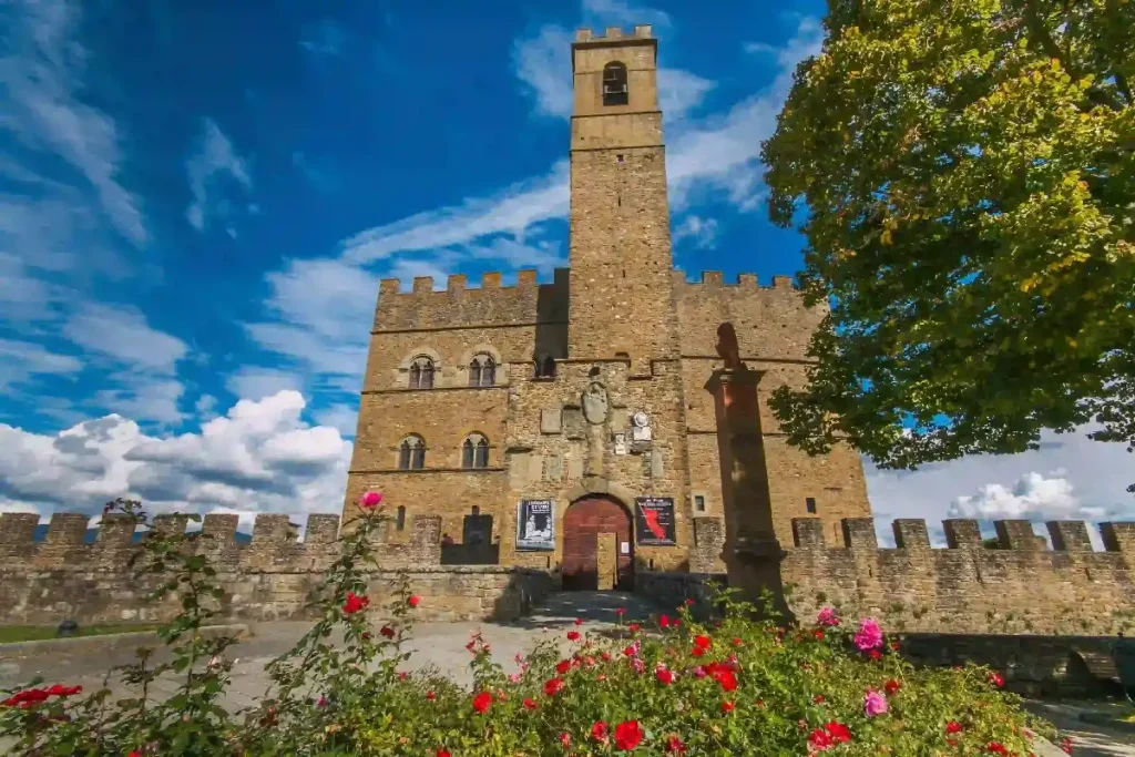 Historic stone castle with a tall tower, surrounded by vibrant flowers and a blue sky. Perfect for sightseeing.