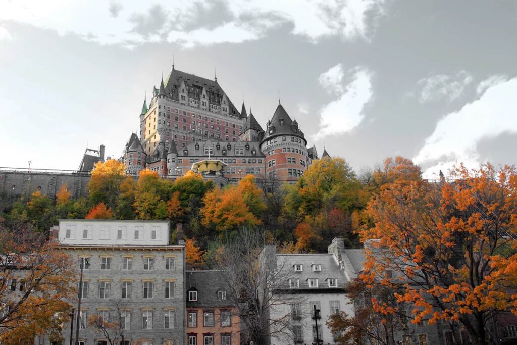 Château Frontenac in autumn, Quebec City; iconic castle-style hotel with vibrant fall foliage and cloudy sky background.