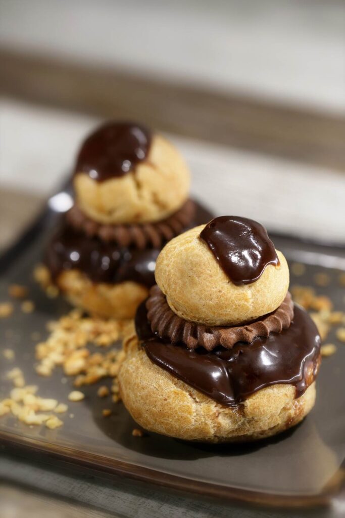 Chocolate profiteroles with rich glaze on a plate, garnished with chopped nuts. Delicious dessert presentation.