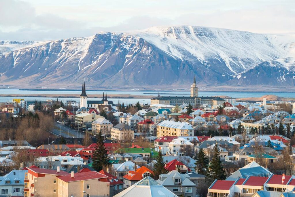 Colorful Reykjavik rooftops with snow-capped mountains in the background, overlooking a calm sea.