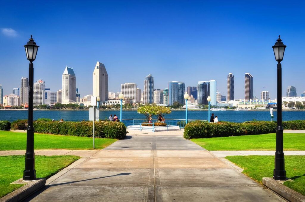 Scenic view of San Diego skyline across the bay with clear blue sky and vibrant green park in the foreground.