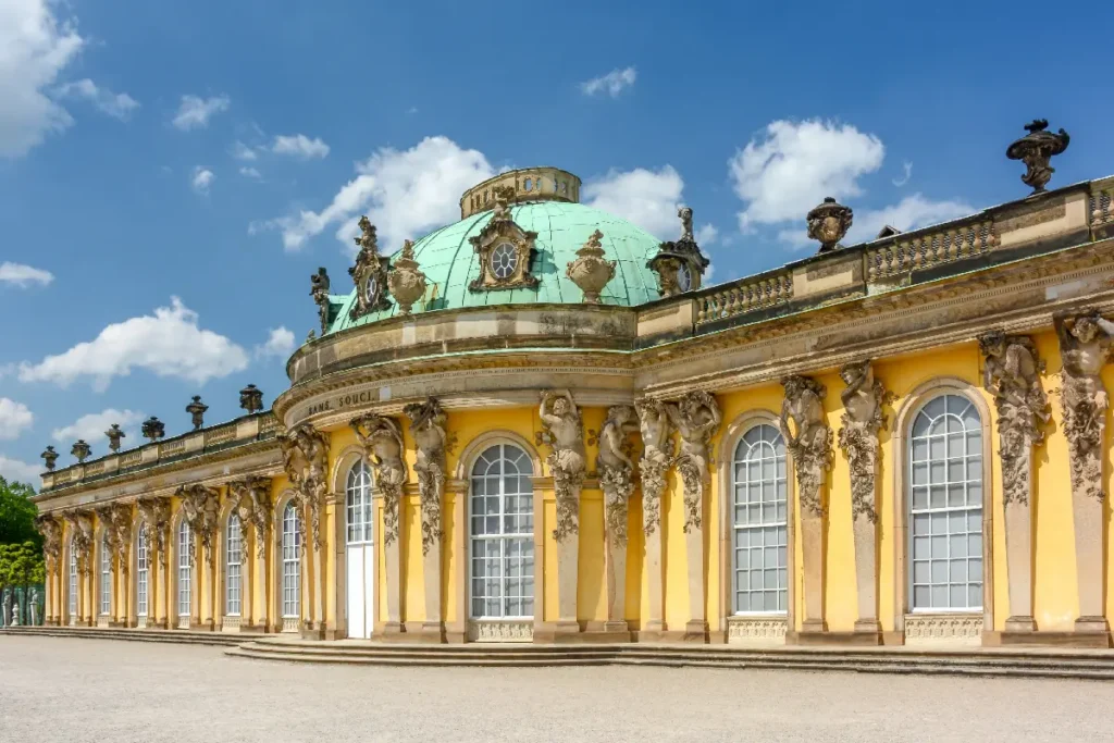 Historic Sanssouci Palace in Potsdam, showcasing stunning yellow facades and a striking green dome under a blue sky.