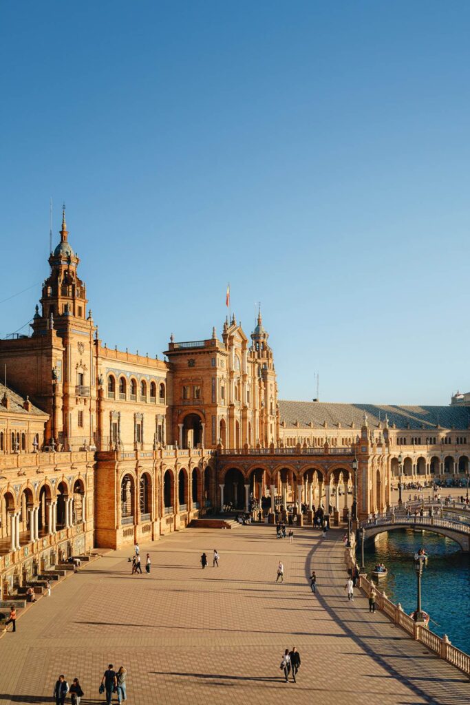Plaza de España in Seville with people and blue sky, showcasing historic architecture and scenic views.